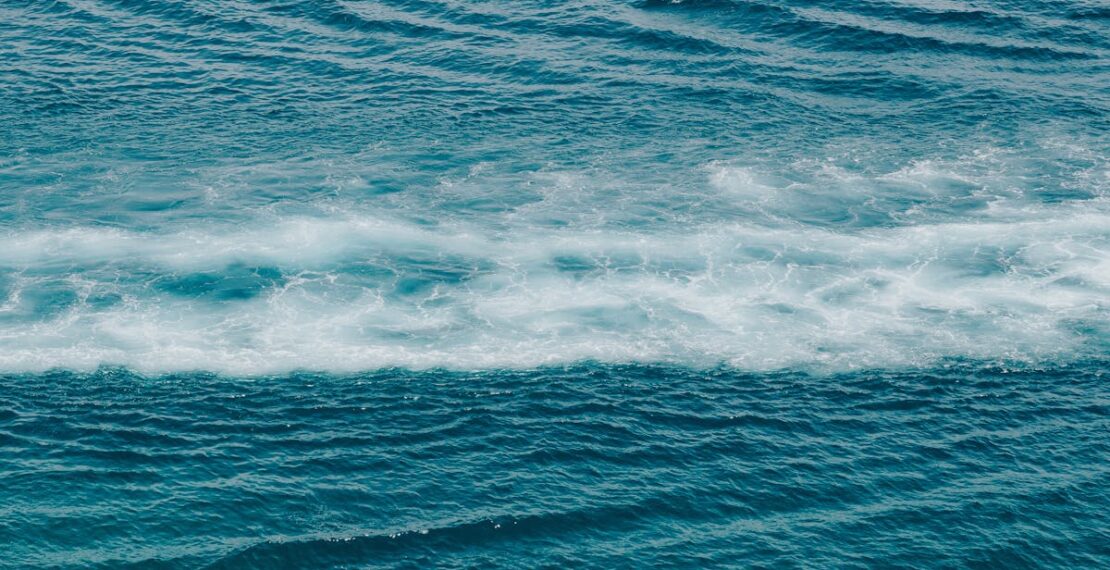 A tranquil ocean scene with gentle waves and foamy white patterns, captured during the day.