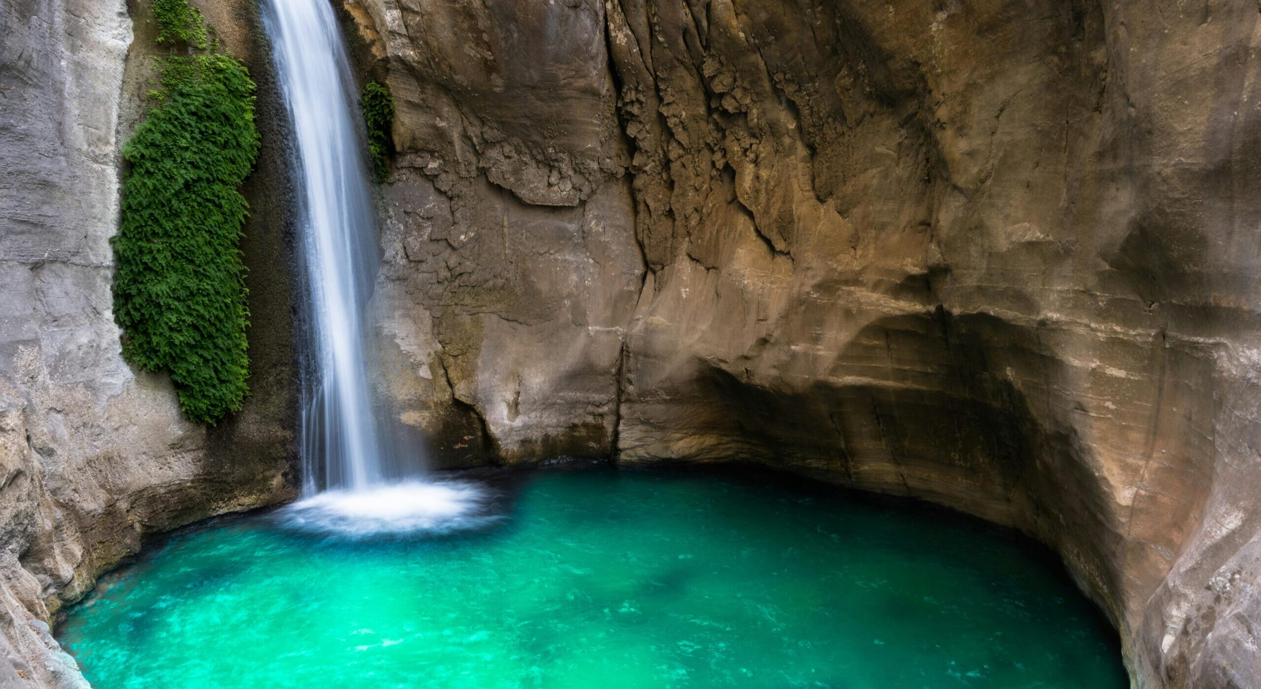 A beautiful waterfall flows into an emerald pool inside a rocky cave, creating a serene natural scene.